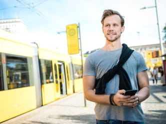 Mann am Handy, im Hintergrund eine Haltestelle