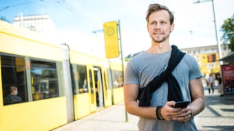 Mann am Handy, im Hintergrund eine Haltestelle