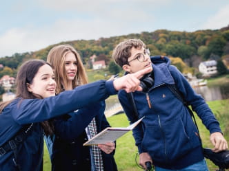 drei Jugendliche an der Elbe mit einem Geocaching-Heft in der Hand