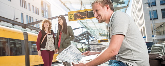 The photo shows a man at a stop with a printed network map in his hand.