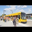 Stop with people and a yellow tram in front of Messe Dresden trade fair glass façade