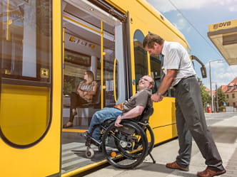 Foto eines Mannes, welcher einem Rollstuhlfahrer beim Einstieg in Straßenbahn hilft