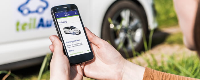 Photo of a hand with a smartphone in front of a teilAuto vehicle