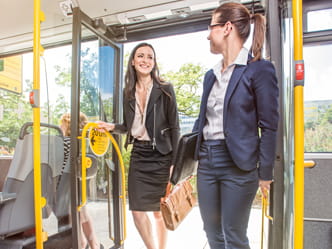 Das Foto zeigt zwei Geschäftsfrauen, welche in einen Bus einsteigen.