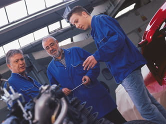 Das Foto zeigt drei Kfz-Monteure in einer Werkstatt.