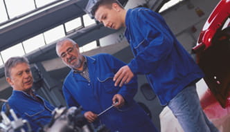 Drei Männer stehen zusammen in blauer Kleidung in einer Werkstattumgebung