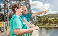 The photo shows a couple standing on the Blue Wonder bridge looking at the Elbe.